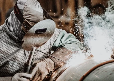 A welder in protective gear with bright sparks and smoke emitting from the welding point.