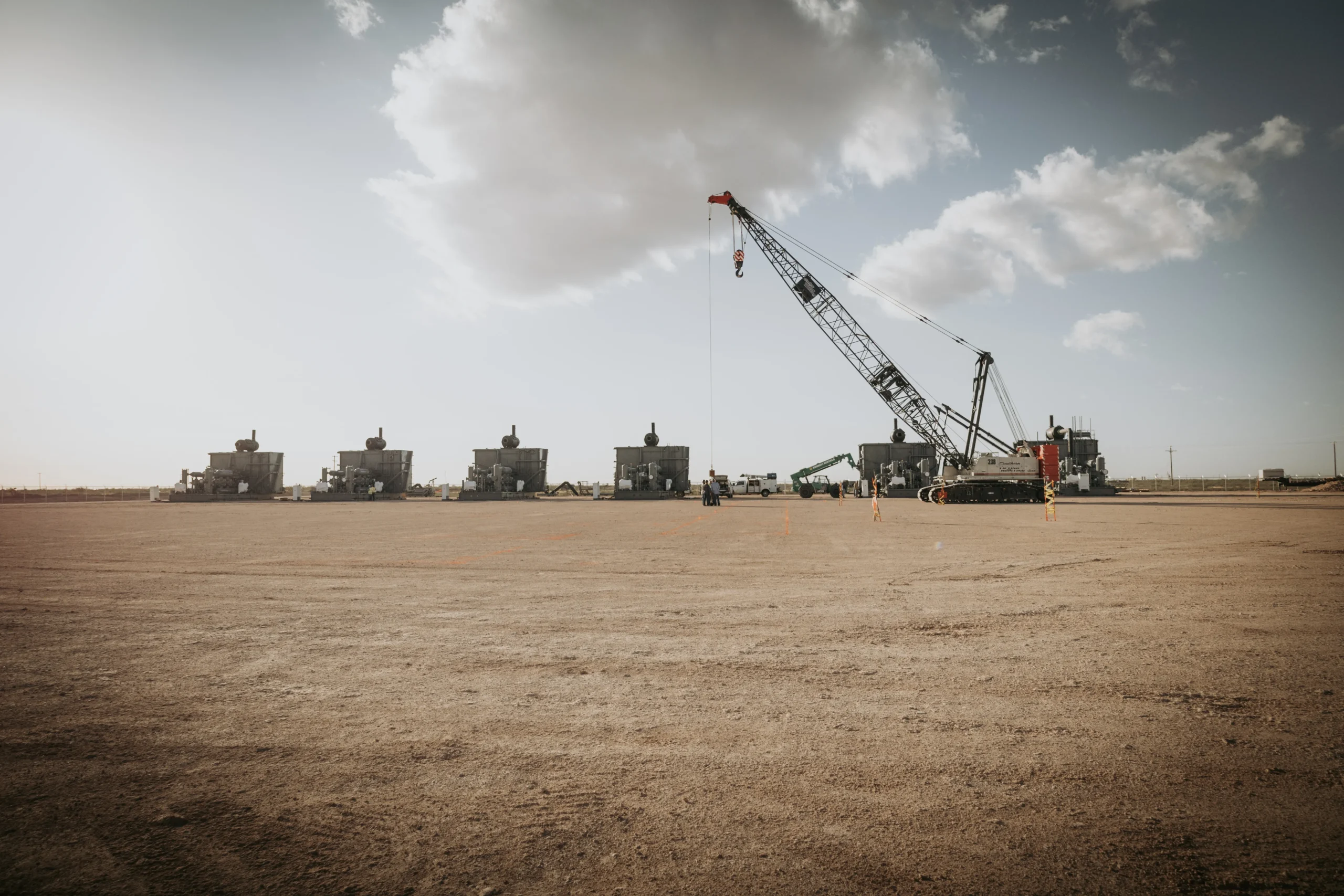 Construction site featuring a large crane and multiple industrial tanks, under a clear sky with scattered clouds.