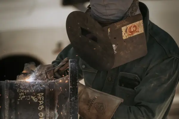 A welder in protective gear works on a metal piece, sparks flying in the air, showcasing craftsmanship and safety in welding.