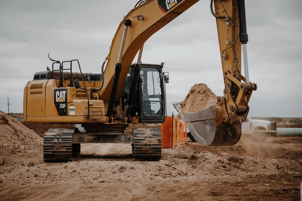 A CAT 330F excavator digging up sandy soil on a construction site under overcast skies.