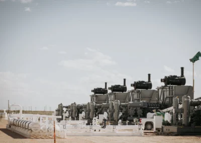 A gas processing site featuring multiple large engines and machinery under a clear sky, with a worker walking nearby.